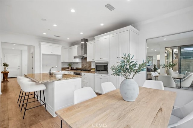 156 Barrow, Irvine, CA 92620 - kitchen featuring wall chimney range hood, a kitchen island with sink, a sink, white cabinetry, and recessed lighting