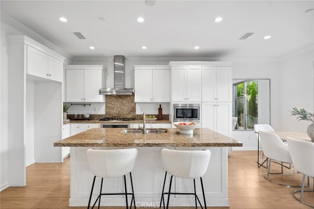 156 Barrow, Irvine, CA 92620 - kitchen featuring wall chimney exhaust hood, a sink, stainless steel microwave, an island with sink, and tasteful backsplash