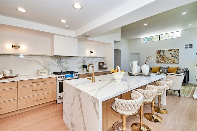 9539 Gladbeck Ave, Northridge, CA 91324 - kitchen featuring stainless steel gas range oven, light wood-style flooring, light brown cabinetry, light stone counters, and a kitchen bar