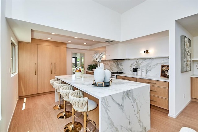 9539 Gladbeck Ave, Northridge, CA 91324 - kitchen featuring light wood finished floors, a kitchen island, a breakfast bar area, light stone countertops, and modern cabinets