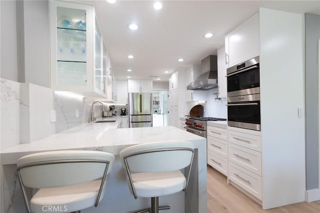 24336 Hillview Dr, Laguna Niguel, CA 92677 - kitchen with appliances with stainless steel finishes, wall chimney exhaust hood, white cabinets, light wood finished floors, and a peninsula