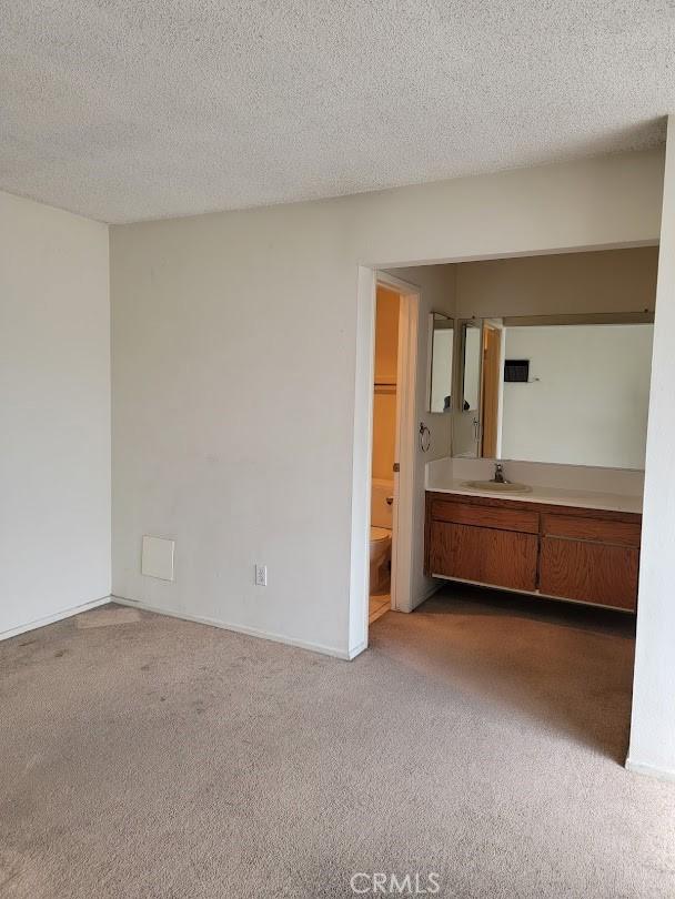 1582 Mitchell Ave, Tustin, CA 92780 - unfurnished bedroom featuring dark colored carpet, a sink, ensuite bath, and a textured ceiling
