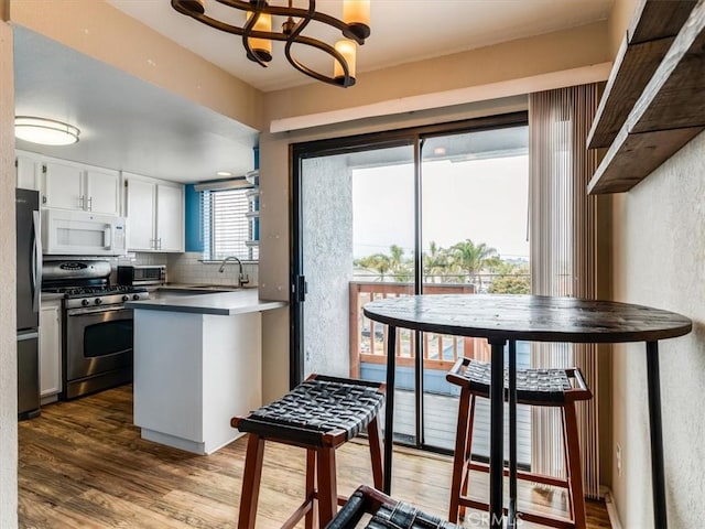 1617 Ramona, Grover Beach, CA 93433 - kitchen with appliances with stainless steel finishes, white cabinets, tasteful backsplash, a chandelier, and wood finished floors