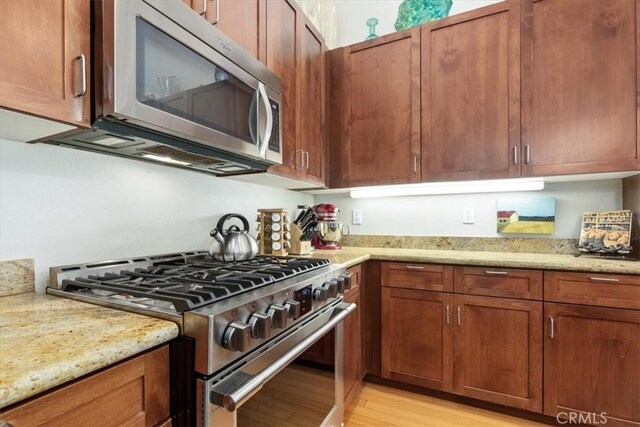 223 San Miguel St, Avila Beach, CA 93424 - kitchen with appliances with stainless steel finishes, light wood-style flooring, light stone countertops, and brown cabinetry