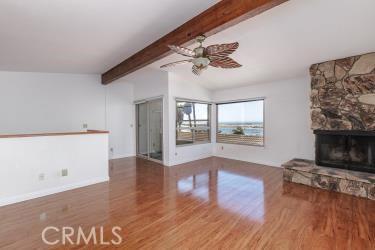 965 Morro Ave Unit D, Morro Bay, CA 93442 - unfurnished living room featuring wood finished floors, beamed ceiling, a ceiling fan, a fireplace, and baseboards