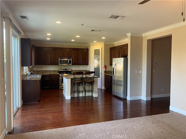 538 Burnt Ranch Way, Chico, CA 95973 - kitchen featuring appliances with stainless steel finishes, a breakfast bar area, a center island, dark brown cabinetry, and ornamental molding