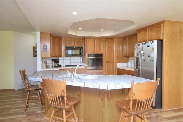 19180 Osceola Rd, Apple Valley, CA 92307 - kitchen featuring appliances with stainless steel finishes, tile countertops, a peninsula, tasteful backsplash, and light wood-style flooring