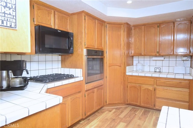 19180 Osceola Rd, Apple Valley, CA 92307 - kitchen with black microwave, stainless steel oven, gas stovetop, tile counters, and light wood-style flooring