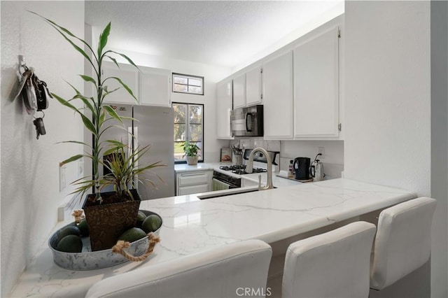 28215 Paseo El Siena Unit 46, Laguna Niguel, CA 92677 - kitchen with black microwave, freestanding refrigerator, white cabinetry, light stone countertops, and white range with gas cooktop