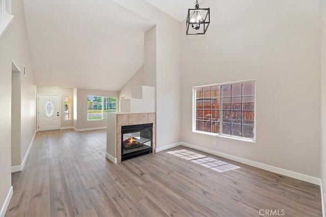 27541 Vanilla Ct, Menifee, CA 92585 - unfurnished living room with wood finished floors, baseboards, a chandelier, a tiled fireplace, and high vaulted ceiling