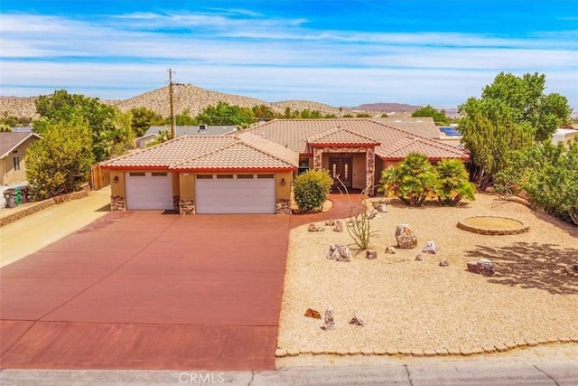 57934 Juarez Dr, Yucca Valley, CA 92284 - mediterranean / spanish house featuring a tiled roof, concrete driveway, a garage, and stone siding