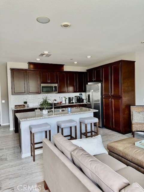 40265 Calle Real, Murrieta, CA 92563 - kitchen featuring stainless steel appliances, light stone counters, a kitchen bar, a kitchen island with sink, and light wood-style floors
