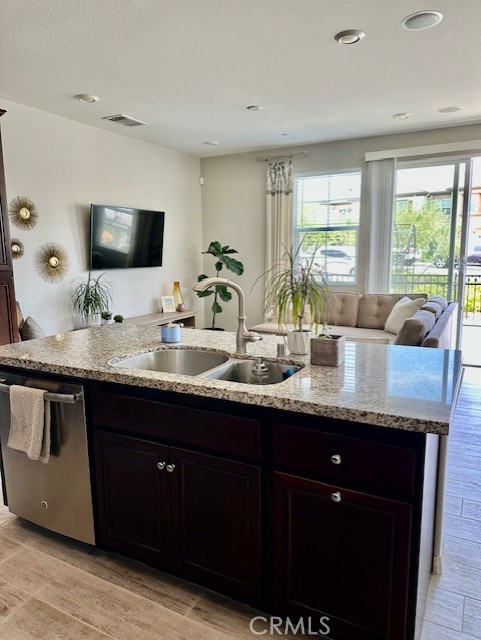 40265 Calle Real, Murrieta, CA 92563 - kitchen with a sink, stainless steel dishwasher, open floor plan, light stone countertops, and a center island with sink