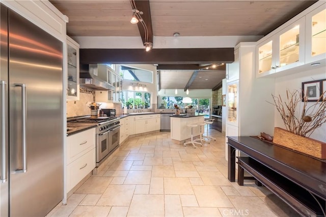 4314 Coronet Dr, Encino, CA 91316 - kitchen featuring premium appliances, wall chimney range hood, wooden ceiling with exposed beams, dark countertops, and stone tile flooring