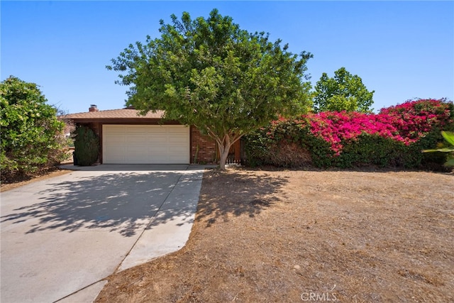 4271 Baggett Dr, Riverside, CA 92505 - obstructed view of property featuring an attached garage, concrete driveway, brick siding, and a chimney