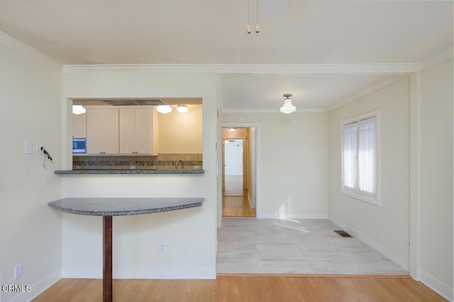 3115 Evelyn St, La Crescenta, CA 91214 - kitchen featuring stainless steel microwave, backsplash, dark countertops, crown molding, and light wood-style floors