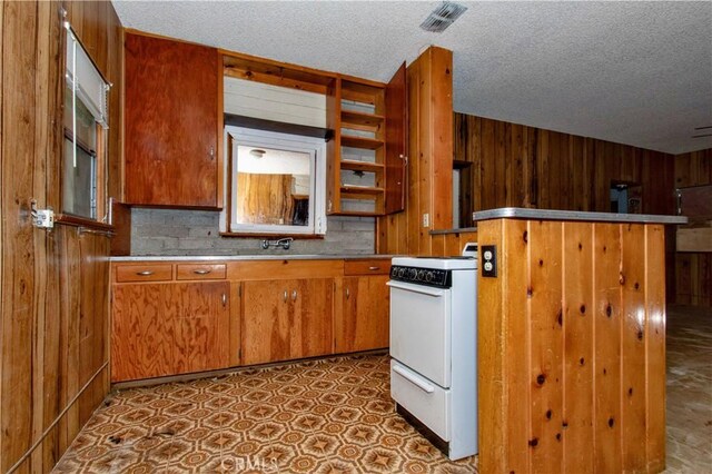 62853 Desert Trail Dr, Joshua Tree, CA 92252 - kitchen featuring white range with electric cooktop, wooden walls, a textured ceiling, brown cabinets, and light countertops