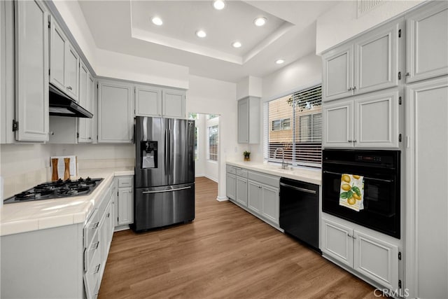 27472 Swallow Ct, Temecula, CA 92591 - kitchen featuring black appliances, recessed lighting, a tray ceiling, light wood-style floors, and tile countertops
