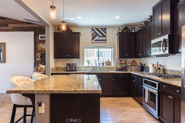 24802 Sandy Trail Pl, Menifee, CA 92584 - kitchen with stainless steel appliances, wood walls, light stone countertops, a kitchen breakfast bar, and a center island