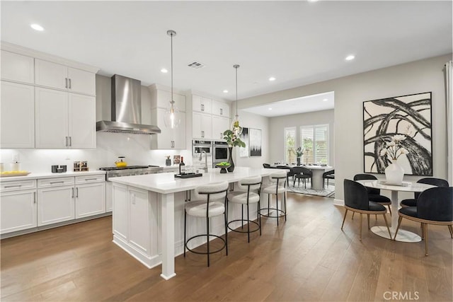 370 Sawbuck, Irvine, CA 92618 - kitchen with wall chimney exhaust hood, wood finished floors, white cabinetry, a kitchen breakfast bar, and recessed lighting