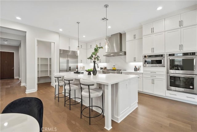 370 Sawbuck, Irvine, CA 92618 - kitchen with stainless steel appliances, wall chimney range hood, light countertops, a breakfast bar, and wood finished floors
