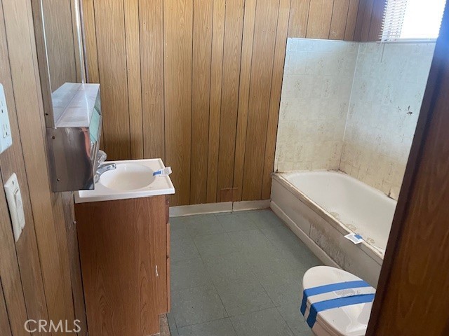 100 Aliso St, Needles, CA 92363 - bathroom featuring a bathtub, vanity, wood walls, toilet, and tile patterned floors