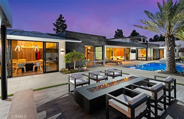 15 Torrey Pines Ln, Newport Beach, CA 92660 - back of property at dusk with an outdoor pool, an outdoor living space with a fire pit, a standing seam roof, a patio area, and stone siding