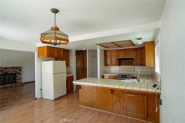 3117 Andre Ln, Turlock, CA 95382 - kitchen with freestanding refrigerator, under cabinet range hood, a peninsula, light wood-style floors, and brown cabinetry