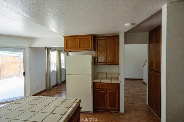 3117 Andre Ln, Turlock, CA 95382 - kitchen with tile countertops, freestanding refrigerator, wood finished floors, brown cabinetry, and a textured ceiling