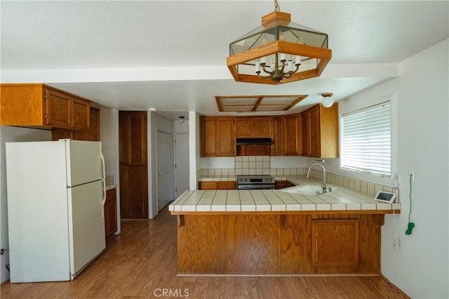 3117 Andre Ln, Turlock, CA 95382 - kitchen with freestanding refrigerator, electric range, a peninsula, under cabinet range hood, and brown cabinetry