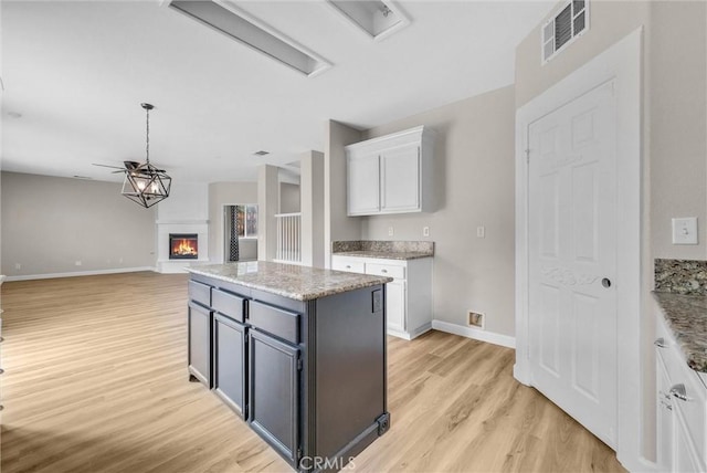 46186 Via Ln, Tranquila, Temecula, CA 92592 - kitchen featuring white cabinets, light wood finished floors, a glass covered fireplace, baseboards, and open floor plan
