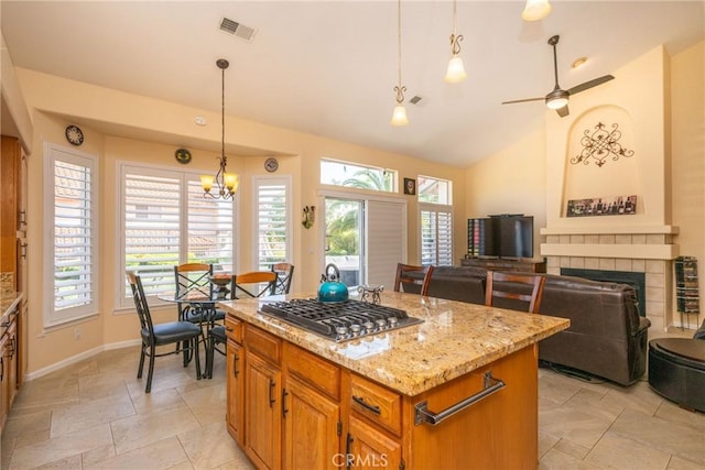 31436 Corte Sonora, Temecula, CA 92592 - kitchen with stainless steel gas stovetop, a tiled fireplace, light stone countertops, vaulted ceiling, and a kitchen island