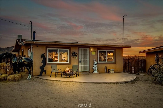1910 Artesia Ave, Landers, CA 92285 - back of house at dusk featuring an outdoor fire pit, a patio area, and stucco siding