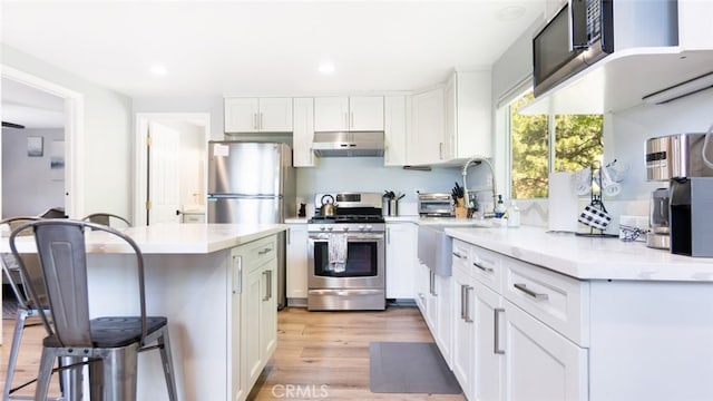 27638 St Bernard Ln, Lake Arrowhead, CA 92352 - kitchen with stainless steel appliances, under cabinet range hood, a kitchen bar, white cabinetry, and recessed lighting