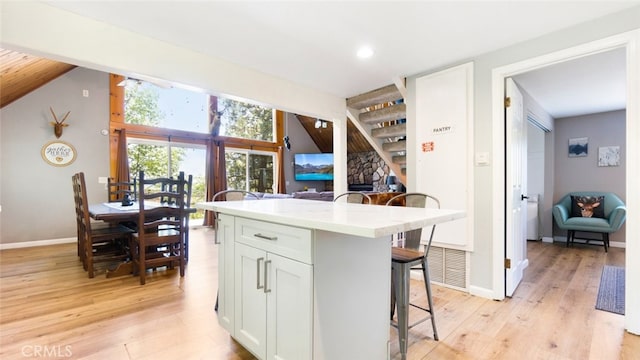 27638 St Bernard Ln, Lake Arrowhead, CA 92352 - kitchen featuring a breakfast bar, light wood-style floors, white cabinetry, a kitchen island, and light countertops
