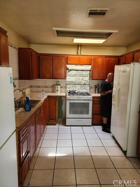 14680 Upland Ave, Fontana, CA 92335 - kitchen featuring white appliances, under cabinet range hood, a sink, light tile patterned floors, and backsplash