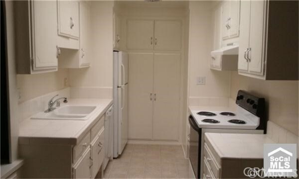 2119 Via Puerta Unit Q, Laguna Woods, CA 92637 - kitchen featuring white appliances, under cabinet range hood, a sink, light countertops, and light tile patterned flooring