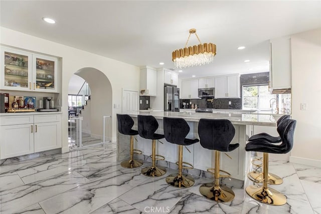 20128 Cavern Ct, Saugus, CA 91390 - kitchen with stainless steel appliances, light marble finish flooring, decorative backsplash, arched walkways, and white cabinetry