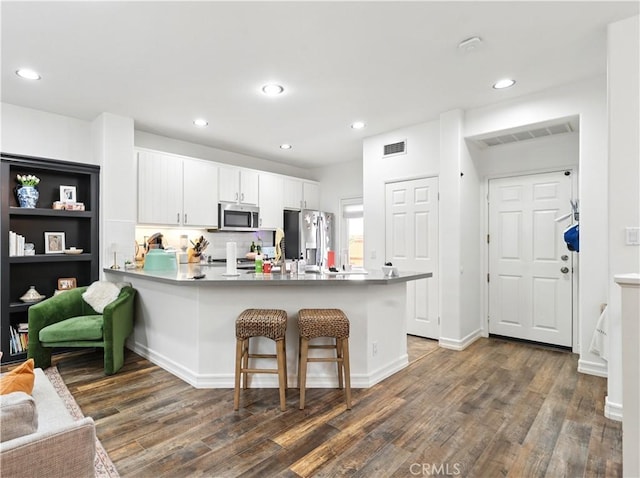 3 Bluff Cove Dr, Aliso Viejo, CA 92656 - kitchen featuring appliances with stainless steel finishes, a peninsula, dark wood finished floors, a kitchen bar, and white cabinetry