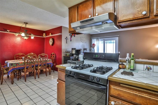3012 Homer Cir, Jurupa Valley, CA 91752 - kitchen featuring gas range, under cabinet range hood, tile counters, light tile patterned flooring, and brown cabinetry