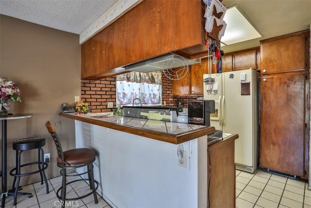 3012 Homer Cir, Jurupa Valley, CA 91752 - kitchen with a peninsula, light tile patterned floors, a kitchen breakfast bar, white refrigerator with ice dispenser, and a textured ceiling