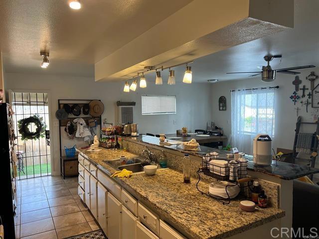 2840 Ridgeway Dr, National City, CA 91950 - kitchen with ceiling fan, light tile patterned floors, fridge, white cabinets, and light stone counters