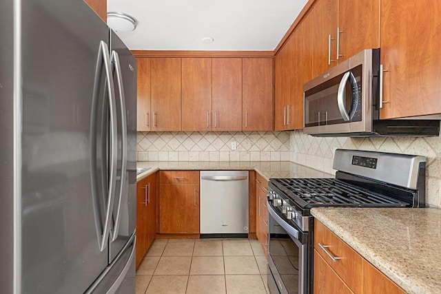 575 7th St # 203, Imperial Beach, CA 91932 - kitchen with stainless steel appliances, brown cabinetry, light tile patterned flooring, tasteful backsplash, and light stone countertops