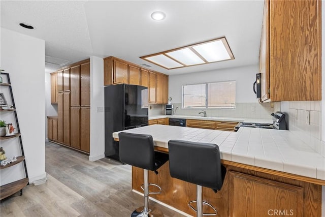 356 Myrl Pl, Hemet, CA 92545 - kitchen featuring black appliances, a peninsula, brown cabinets, light wood finished floors, and decorative backsplash
