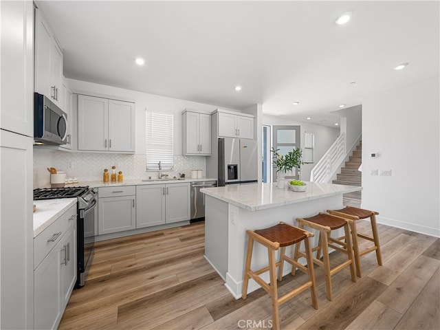 191 Lynx, Irvine, CA 92618 - kitchen featuring stainless steel appliances, a breakfast bar area, backsplash, a center island, and light wood-type flooring