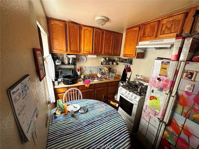 1136 Arapahoe St, Los Angeles, CA 90006 - kitchen with white range with gas cooktop, freestanding refrigerator, brown cabinetry, under cabinet range hood, and light countertops