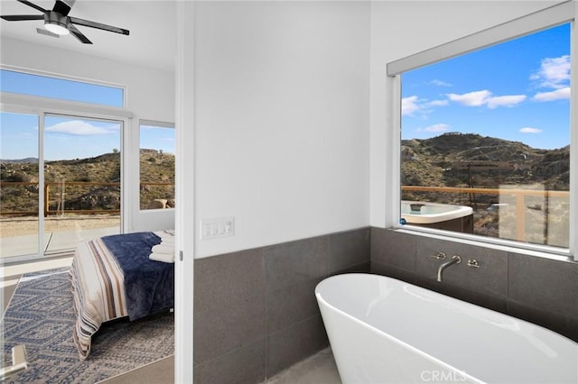 5890 Olema Rd, Yucca Valley, CA 92284 - bathroom featuring a mountain view, a freestanding bath, tile walls, a ceiling fan, and wainscoting