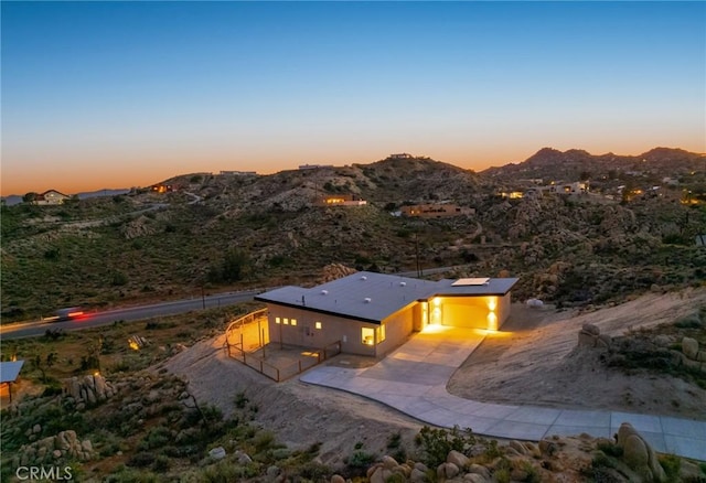 5890 Olema Rd, Yucca Valley, CA 92284 - back of house at dusk with concrete driveway, a mountain view, a patio, and a garage
