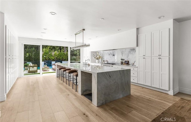 5 Modesto, Irvine, CA 92602 - kitchen featuring light wood-style flooring, a large island with sink, tasteful backsplash, white cabinetry, and recessed lighting