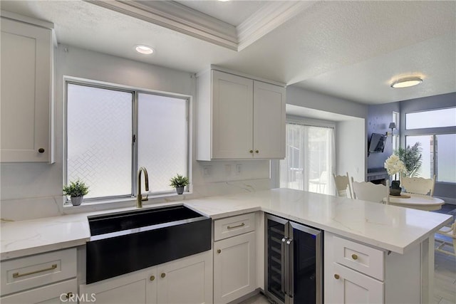 13365 Cloudburst Dr, Corona, CA 92883 - kitchen with beverage cooler, a peninsula, ornamental molding, light stone counters, and white cabinetry